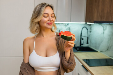 A sensual woman enjoys a slice of juicy watermelon in a modern kitchen. Confident, playful, and...