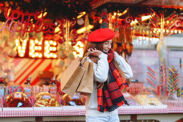 Woman in red beret enjoys shopping at a festive market during winter, surrounded by colorful decorations and cheerful atmosphere in the evening
