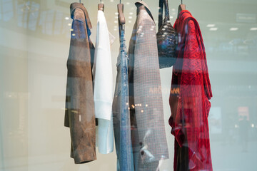 A row of stylish clothes and accessories hanging in a modern store display behind glass