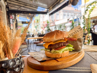 A juicy cheeseburger with bacon, lettuce, and tomato served on a wooden plate in an outdoor cafe