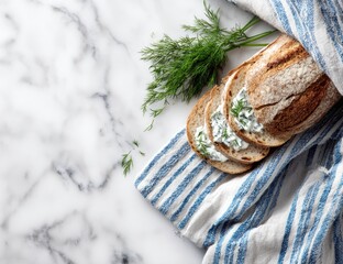 Sliced crusty bread topped with creamy dill spread, rests on a blue and white striped kitchen towel atop a marble surface. Fresh dill sprigs are arranged nearby