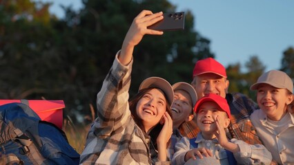 Happy travelers taking photos on smartphone at halt laughing hugging friend. Family trip with backpacks in nature. Team of travelers, rest stop, video bloggers. Team of tourists on vacation nature