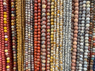 A display of assorted natural stone beads in various earthy tones arranged in strands