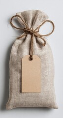 A light beige linen sack, tied with twine, features a blank brown tag.  The rustic, simple packaging is photographed against a neutral backdrop