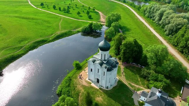 Bogolyubova, Russia - May 13, 2024: A high-angle drone shot of the Church of the Intercession on the Nerl, located at the bend of a river surrounded by lush green meadows
