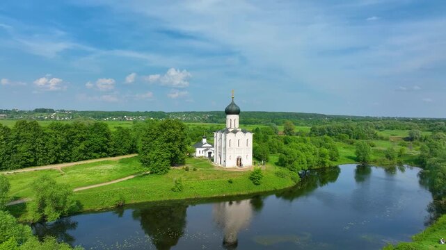 Bogolyubova, Russia - May 13, 2024: A close-up aerial shot of the Church of the Intercession on the Nerl, situated by a tranquil river, with pathways and trees surrounding it