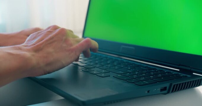 Close-up of female hands typing on laptop keyboard at home. Green screen on monitor for customization in video projects