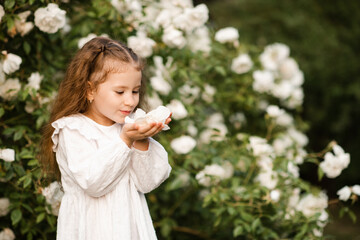Cute child girl 4-5 year old wearing white dress having fun with flowers over nature background in...