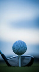Golf ball on tee, driver in foreground, blurred sky background, showcasing a moment of focus and preparation before a golf swing