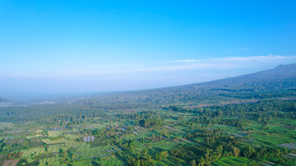 Obraz premium A stunning view of Mount Semeru from the terrace, with green fields, misty valley, and blue sky creating a peaceful and majestic natural scene.