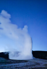 A large geyser is spewing steam into the air on a clear night
