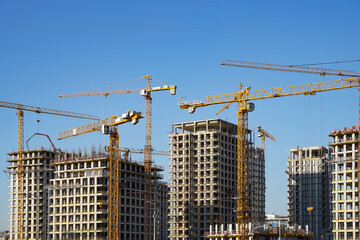 Fototapeta premium Yellow tower cranes working on the new hi-rise residential buildings in the city near the river. 
