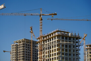 Yellow tower cranes working on the new hi-rise residential buildings in the city near the river. Real estate growth tendency and the new construction industry technology