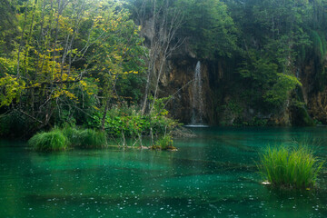 Lush scene of a light stream waterfall and a lake with raindrops on the water at the Plitvice Lakes National Park