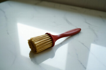 A single red handled paintbrush with golden bristles resting on a white surface with soft shadows and sunlight isolated on transparent background