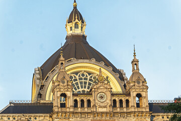 the grand facade of Antwerp Central Station in Belgium, with columns, arches, and sculptural details clock a golden statue, a domed roof  illuminated warmly