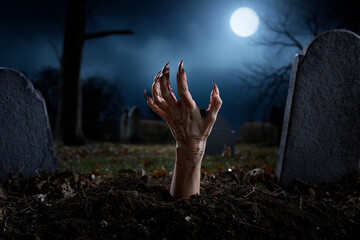 Spooky reanimated monster hand emerging from a grave in a dark, moonlit cemetery.