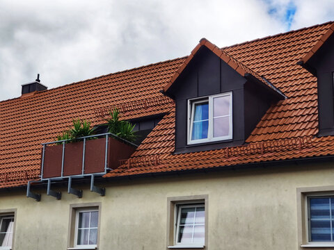 Red tile roof of residential building with attic against blue sky with dense clouds. European architecture. Close-up. Copy space. Selective focus.
