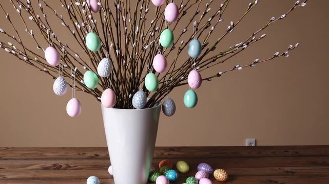 Contemporary arrangement of willow branches adorned with pastel-colored Easter egg ornaments in minimalist white vase
