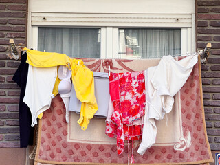 Laundry hanging on balcony rope with colorful clothes and textiles against brick wall. Domestic...