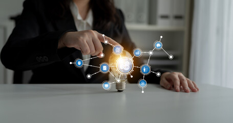 A business person points to a glowing light bulb surrounded by digital icons, symbolizing innovation and the interconnectedness of ideas in a modern office environment. Tessel