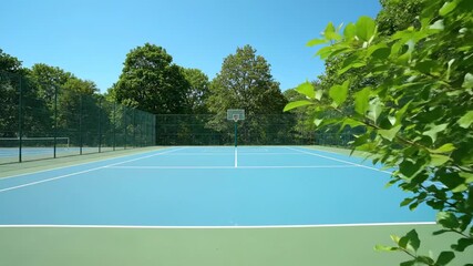 Outdoor Basketball Court Framed by Lush Greenery - A light blue basketball court with white lines is surrounded by a vibrant green fence and lush foliage, creating a refreshing outdoor sports scene - Powered by Adobe