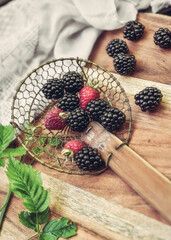 Blackberries and raspberries ready for cooking in a ladle on a wooden board