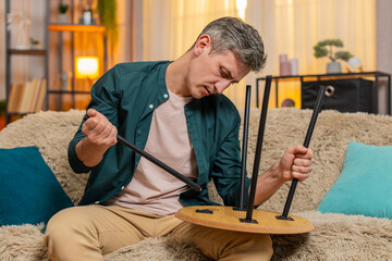 Young man at home repairs small wooden table with calm focus, appearing satisfied with progress and...
