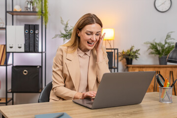 Middle-aged businesswoman at home office on laptop sees system crash data loss holds head facepalm...