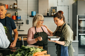 Female chef giving tray to senior woman while teaching in cooking class at commercial kitchen
