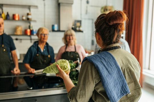 Rear view of female chef holding cabbage while teaching in cooking class at commercial kitchen