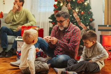 Grandfather explaining christmas traditions to grandchildren near decorated tree