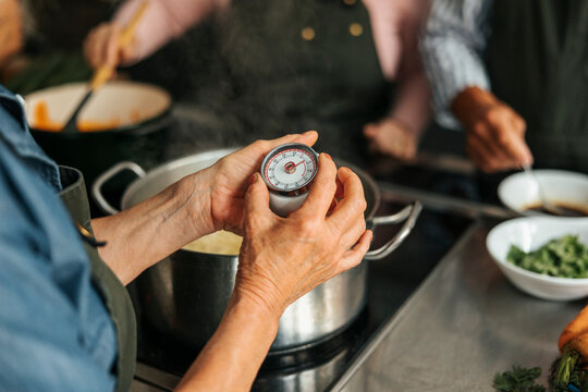 Midsection of senior woman setting timer while cooking in commercial kitchen