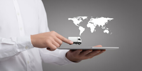 Global delivery and logistics technology. A person in a white shirt holds a tablet with a small van and a world map hovering above.