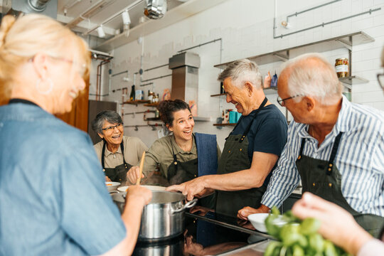 Senior adult students enjoying cooking with chef in commercial kitchen