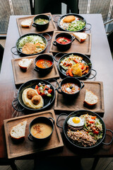 Assorted restaurant-style meals served in black bowls on wooden trays, top view