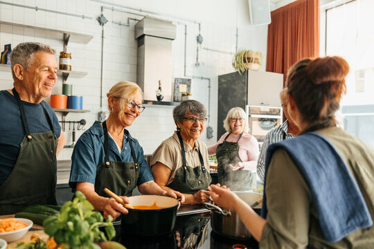 Smiling senior men and women learning from female chef in cooking class at commercial kitchen - Powered by Adobe