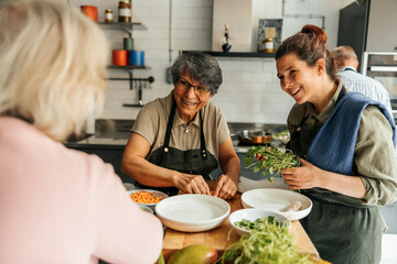 Smiling senior woman making rice paper spring roll with assistance of female chef during cooking class in commercial kit