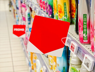 Blank red square shelf label on supermarket aisle fixture for in store promotion, empty price tag...