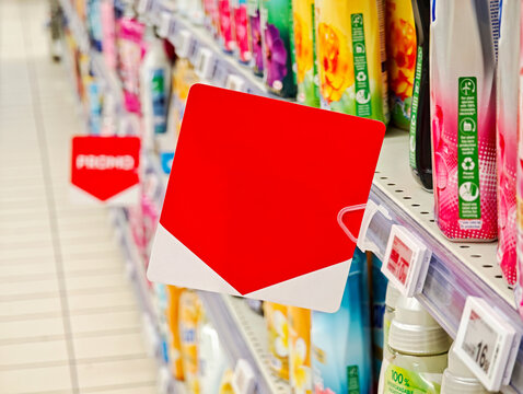 Blank red square shelf label on supermarket aisle fixture for in store promotion, empty price tag signage sign, store shelf, retail products display, copy space, buying selling goods items, no people