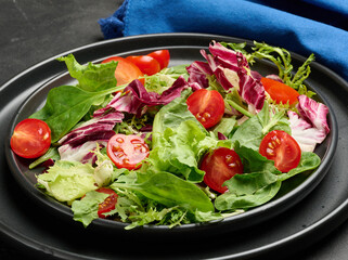 Fresh salad with mixed greens, radicchio and cherry tomatoes, served on a matte black plate.