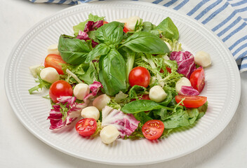 Fresh salad with mixed greens, radicchio and cherry tomatoes, served on a white plate.