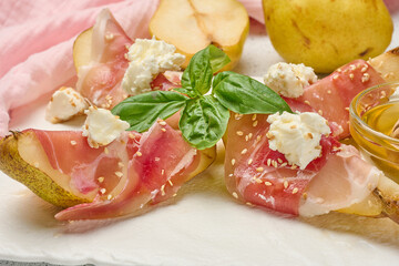 Pear slice wrapped in prosciutto with cheese and sesame seeds on a white board