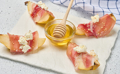Pear slice wrapped in prosciutto with cheese and sesame seeds on a white board