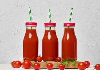 Glass bottles with tomato juice with red caps. Fresh red tomatoes lie on a wooden stand and in...