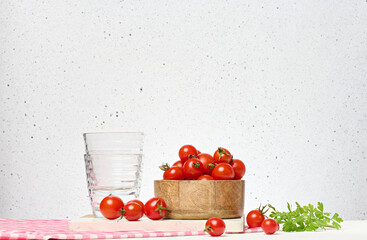 Wooden bowl with red ripe cherry tomatoes and empty glasses on white background