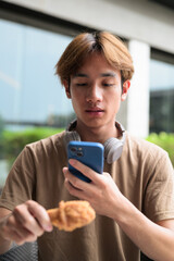 Fototapeta premium Happy man eating and taking photo of fried chicken drumstick outdoors for casual lunch with phone