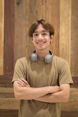 Portrait of young Asian Thai man with headphones against wooden background © Ranta Images