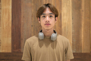 Portrait of young Asian Thai man with headphones against wooden background