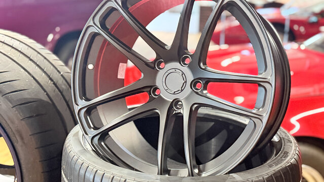 Car alloy wheel on tire, front view close-up in workshop, multi-spoke rim with central hub, product photo with shallow depth of field and blurred background